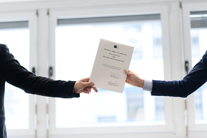 Zwei Arme halten von links und rechts ein Zertifikat für Hochschuldidaktik hoch.