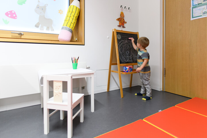 A kindergarten aged boy drawing with chalk on a blackboard.